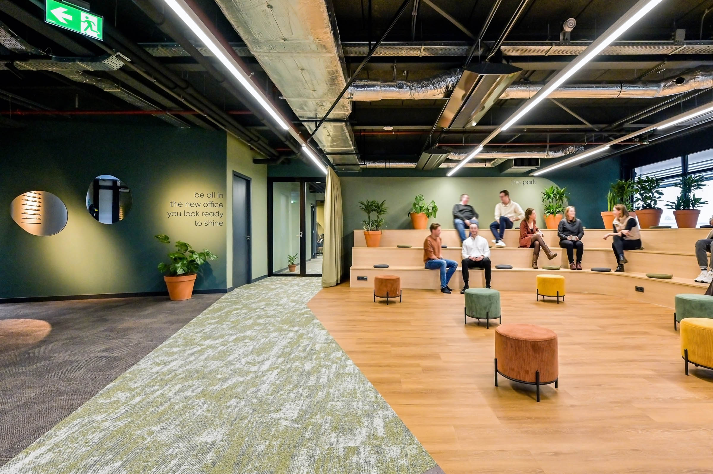 Moderne kantoorruimte met tribune, planten en open plafond bij Zivver kantoorinterieur.